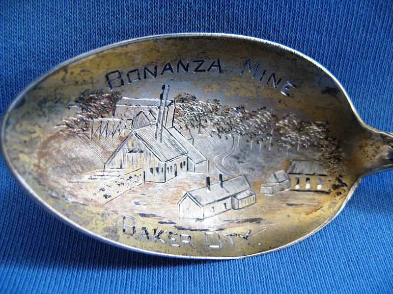 Souvenir Mining Spoon Bonanza Mine Bowl Engraving.JPG - SOUVENIR MINING SPOON BONANZA MINE ROBINSONVILLE OR - Sterling silver spoon with engraved mine scene in gold washed bowl, marked BONANZA MINE BAKER CITY, ca. 1895, marked Sterling with an S maker’s mark on reverse, made by the Shepard Mfg. Co. Melrose Highlands, MA 1893-1923, handle is marked OREGON with 1859 and crest at top, length 5 1/2 in. and weight 20.3 g,  [The Bonanza Gold Mine was the largest and probably the most valuable free gold mine in the Pacific Northwest in the 1890s.  It was located at the head waters of Burnt River at an elevation of 5,140 feet, about four miles southeast of Robinsonville in Baker County, Oregon, or approximately 40 miles west of Baker City. Discovered in 1877 by a pioneer prospector named Jack Haggard, it was worked by the original locators for two years, reducing the quartz and gold vein ores by the arrastra process. In 1879 the Bonanza Mining Co. purchased it, and erected a ten stamp mill. They continued operations, but failed to make a success of it, and finally closed down.  In 1892 the Geiser Company headed by Al Geiser purchased it, reopened the old works and had the mine and mill in continuous operation until it was sold in 1898, producing nearly $3 million in gold over that period as the heaviest producer in the state. The mine continued in operation till 1907 but little is known after that.  Most recently, a Canadian firm named the Marathon Gold Corp. of Toronto bought the Bonanza in 2012 from the Gazelle Land and Timber LLC of Canyon City with plans to conduct exploratory work.]